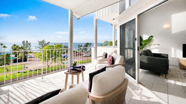 A balcony with a view of the sea, furnished with chairs and a table, and a sliding glass door leading to an indoor area.