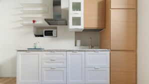 Une cuisine avec des meubles blancs, un four à micro-ondes, une bouilloire et un meuble en bois.