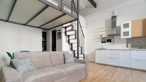 Un salon avec un canapé, un escalier, une cuisine avec des meubles blancs et un four à micro-ondes.