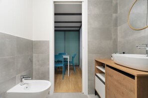 Ein modernes Badezimmer mit einem weißen Waschbecken, einer Holzwaschtischplatte und Blick in einen Essbereich mit blauen Stühlen und einem Tisch.