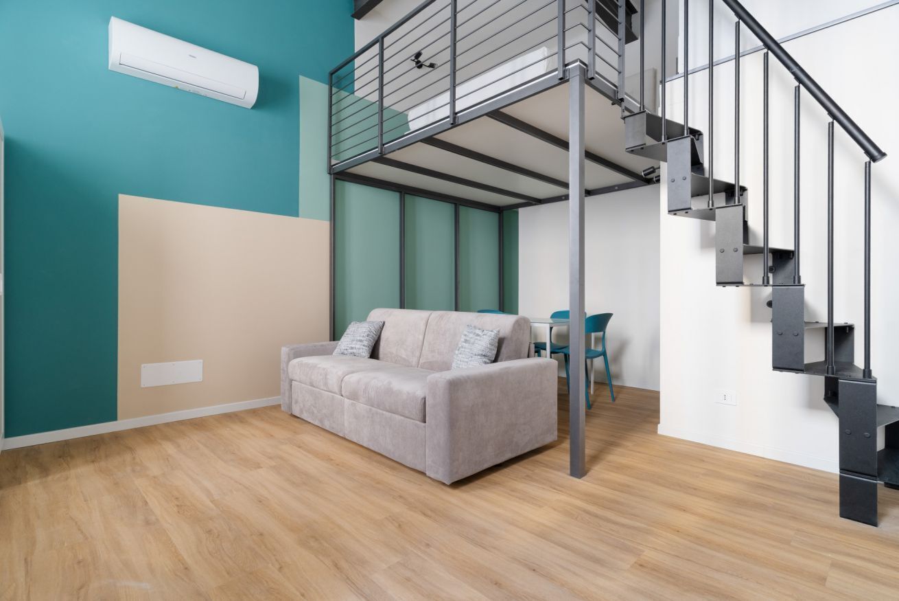 Un intérieur moderne avec un canapé gris, des murs de couleur turquoise, un escalier et un ventilateur de plafond.