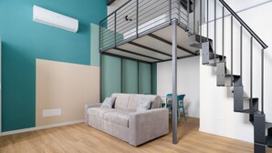 Un intérieur moderne avec un canapé gris, des murs de couleur turquoise, un escalier et un ventilateur de plafond.