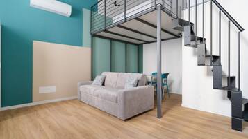 Un intérieur moderne avec un canapé gris, des murs de couleur turquoise, un escalier et un ventilateur de plafond.