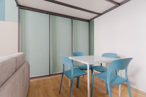 Ein Zimmer mit einem weißen Tisch, vier blauen Stühlen, einem grauen Sofa und einem großen Fenster mit geätzten Glasscheiben.