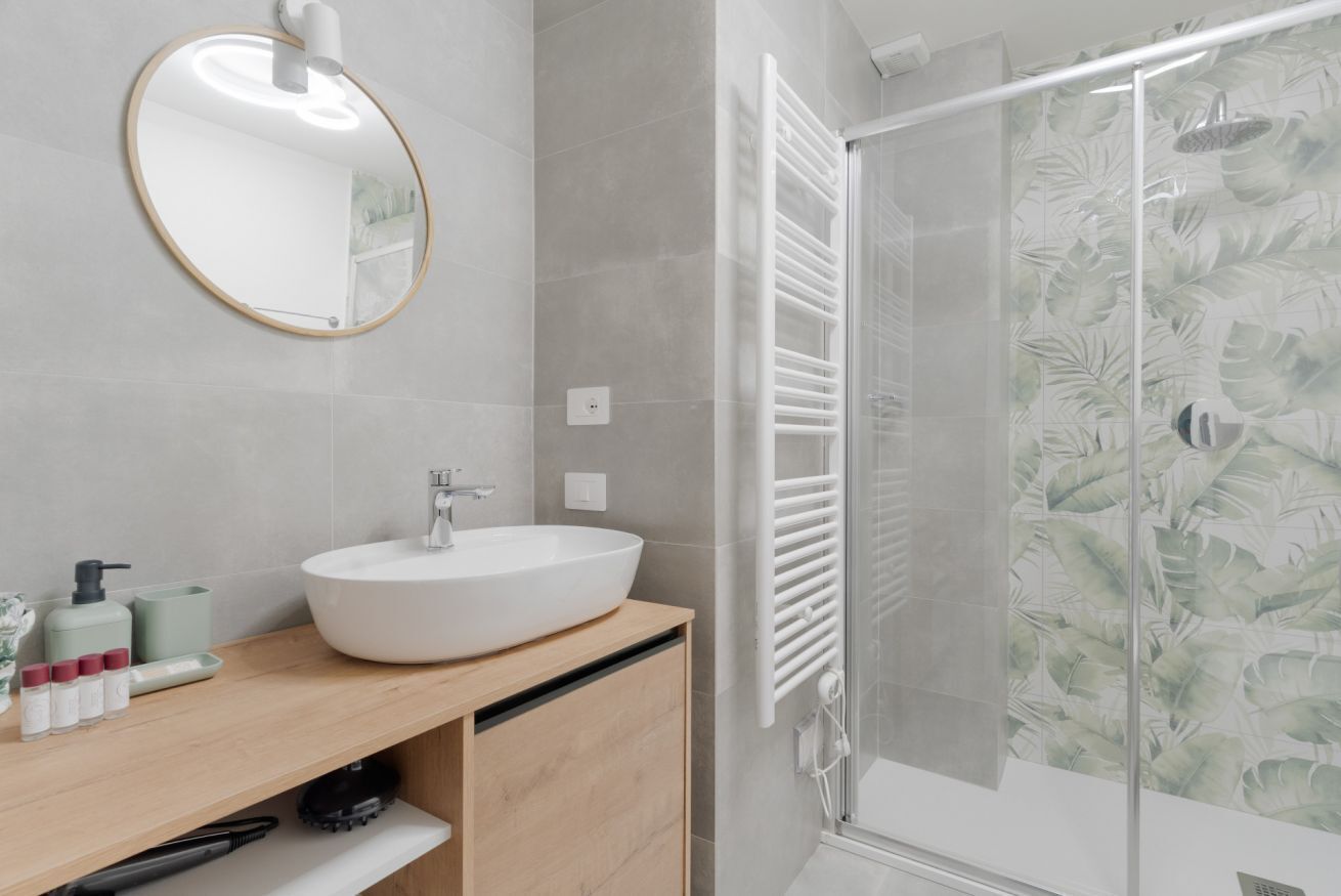 Une salle de bain avec un miroir rond, un lavabo blanc et une cabine de douche en verre.