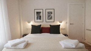 Ett hotellrum med en säng, två inramade tavlor på väggen, en dörr och ett nattduksbord med en lampa.