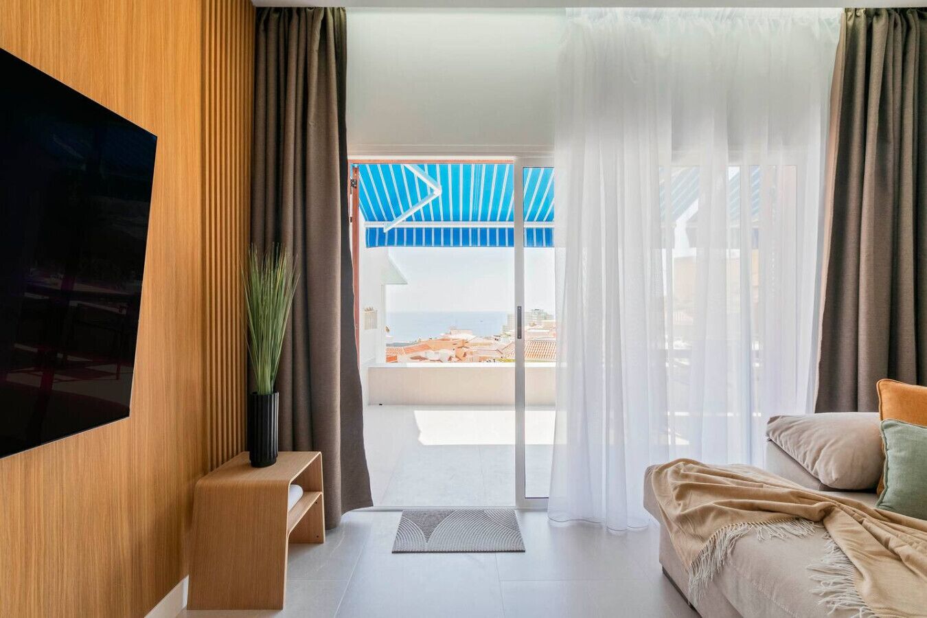 A modern hotel room with a TV, a sofa, a coffee table, and a view of the beach.