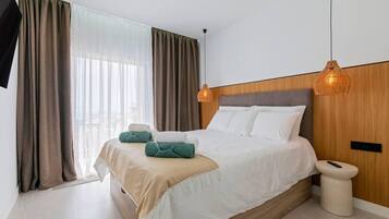 Une chambre d’hôtel moderne avec un grand lit, deux lampes de chevet, une table de chevet et une vue sur la ville grâce à de grandes fenêtres.