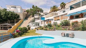 Ein Pool mit geschwungener Kante, eine Treppe zu einem Gebäude und eine kleine Terrasse mit Stühlen.