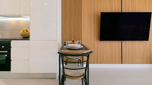 Eine moderne Küche mit weißen Schränken, einer Wand in Holzoptik, einem Esstisch mit Stühlen und einem an der Wand befestigten Flachbildfernseher.
