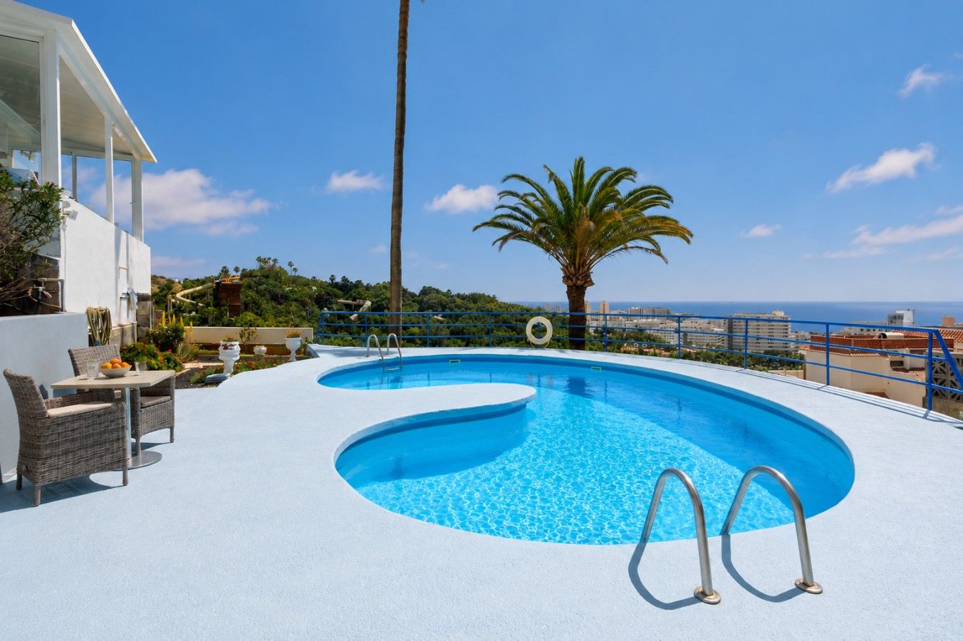 A swimming pool with a view of the sea, surrounded by a white deck and outdoor furniture.