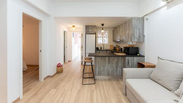 Una cocina moderna con una isla central, un área de comedor con sofá y un pasillo que lleva a otra habitación.