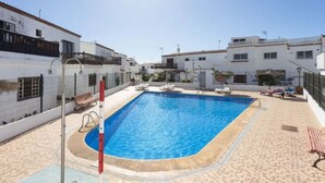 Una piscina rectangular con solárium empedrado, rodeada de edificios blancos con balcones.