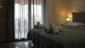 A hotel room with a bed, a nightstand, a lamp, and a view through the window. - Electra (Aigialeia)