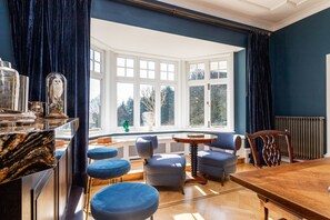 Una habitación con ventanal, una mesa de comedor de madera, sillas tapizadas en azul y una encimera de mármol.