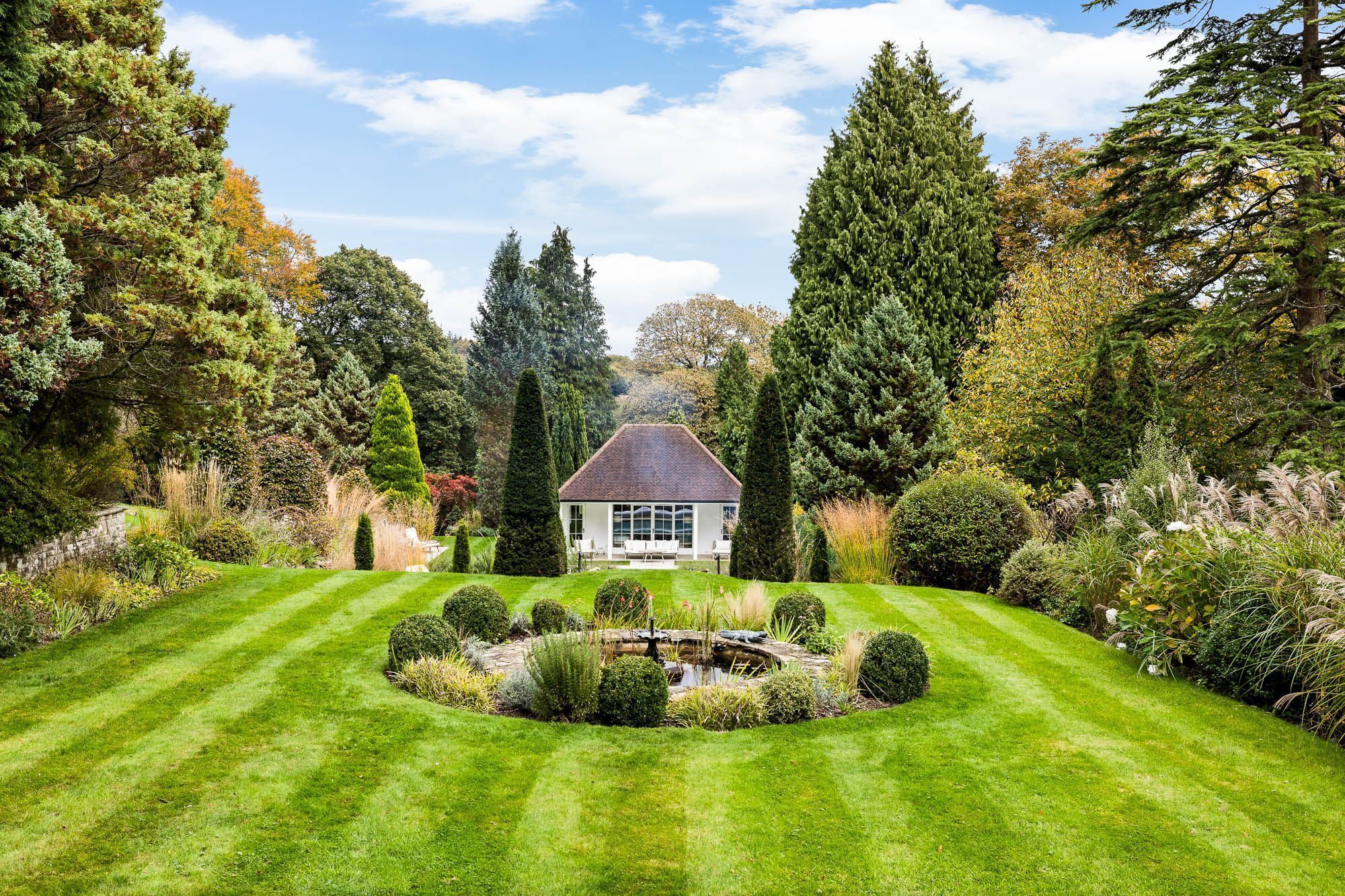 A well-manicured garden with a central pond, surrounded by neatly trimmed hedges and a variety of trees.