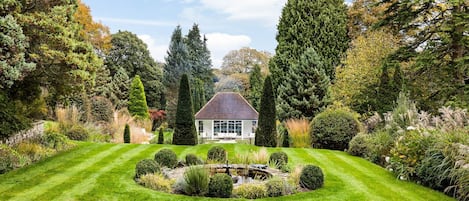 A well-manicured garden with a central pond, surrounded by neatly trimmed hedges and a variety of trees.