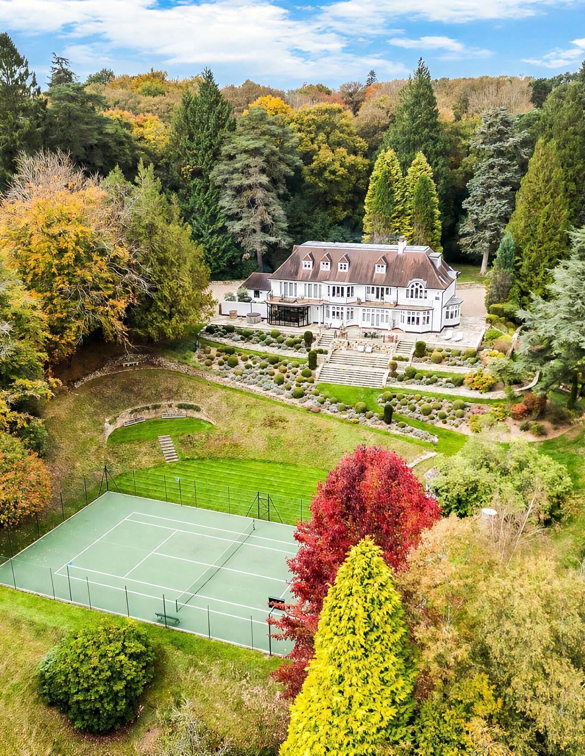 Un vaste domaine comprenant un court de tennis, des jardins aménagés et une grande variété d’arbres.