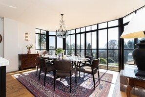 Comedor con una mesa dispuesta para seis personas, rodeada de sillas, una araña y vistas a través de amplios ventanales.