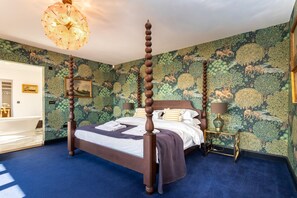 Una cama con dosel de madera oscura, un piso cubierto de moqueta azul y una pared con papel tapiz de motivos naturales.