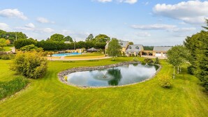 A large house with a swimming pool, a pond, and a well-maintained lawn.