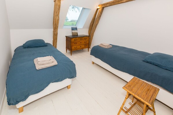 A bedroom with two beds, a wooden dresser, a small table, and a skylight.