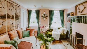 A cozy living room with a sofa, a fireplace, and a large window with curtains.
