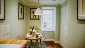 A dining area with a round table, chairs, a vase with flowers, and a window with blinds.
