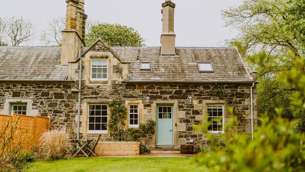 A stone house with a green door, two chimneys, and a small garden.