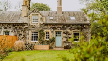A stone house with a green door, two chimneys, and a small garden.