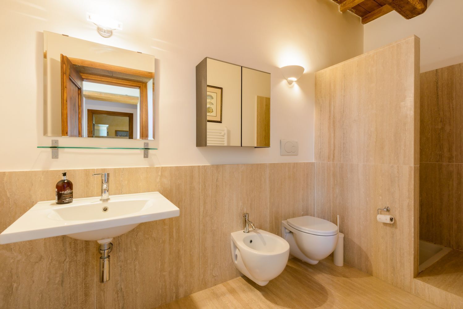 Ein Badezimmer mit Waschbecken, Bidet, Toilette und einem Spiegel mit einem Glasregal darüber.