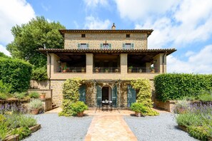 Un bâtiment en pierre de deux étages, doté d’un balcon, d’une terrasse couverte et d’un chemin de gravier.