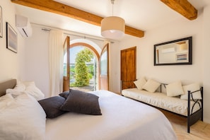 Une chambre à coucher comprenant un lit, un canapé, un luminaire suspendu et une porte en arc donnant sur un espace extérieur.