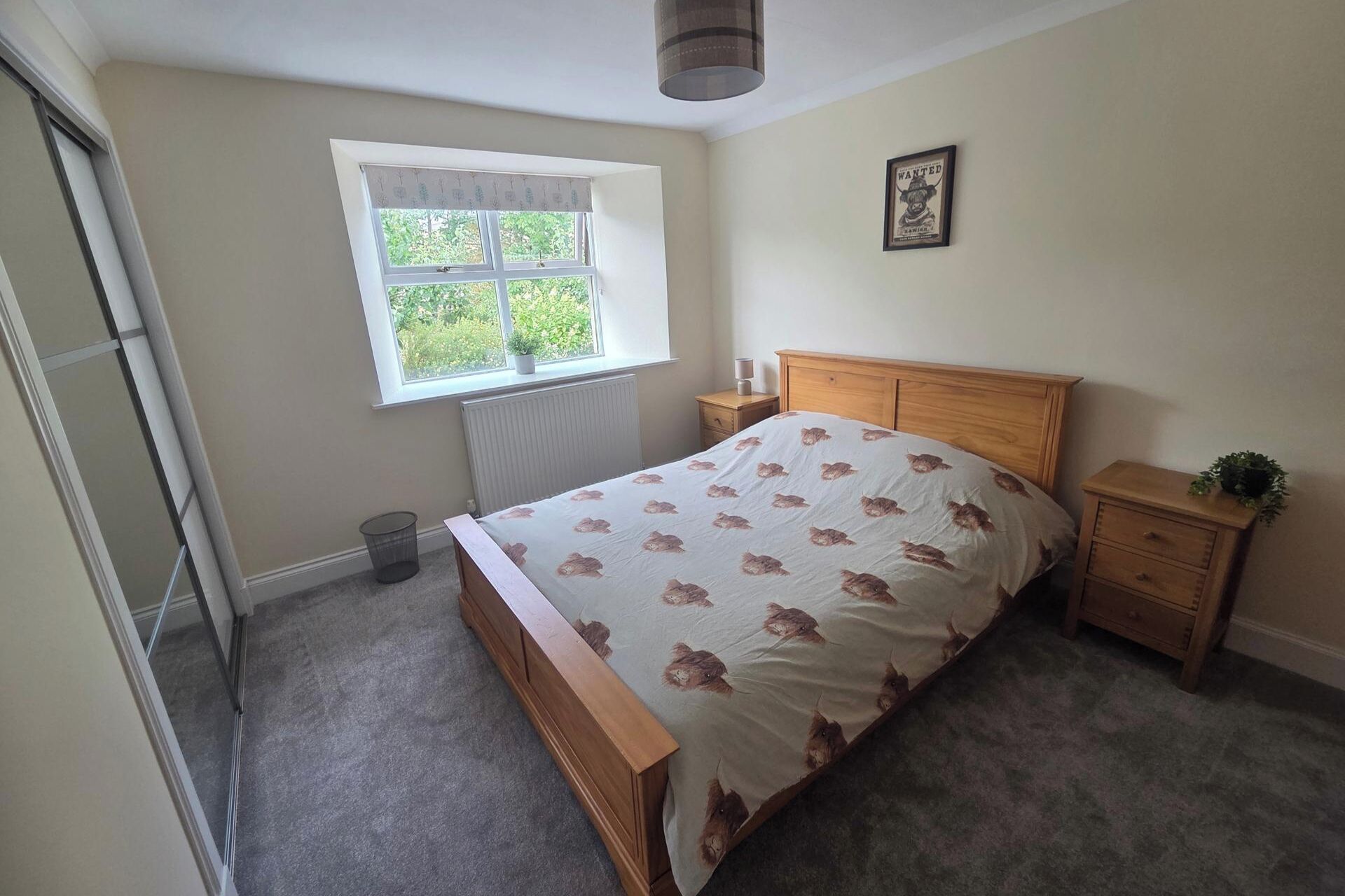 A bedroom with a bed, a window, a radiator, a nightstand, and a framed picture on the wall.