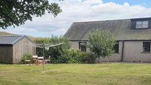 A residential property with a grassy yard, a wooden shed, and a house with a sloped roof. - Farm Cottage at Foot Angus Glens (Kirriemuir)