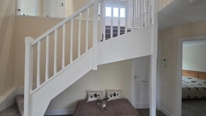 A staircase with white railings leading to a second floor, a bedroom with a bed and two pillows, and a bathroom door. - Farm Cottage at Foot Angus Glens (Kirriemuir)