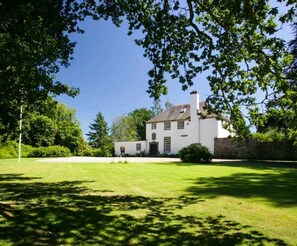 A white building with a traditional design, surrounded by a well-maintained lawn and trees.