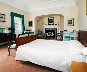 A large bed with a wooden headboard, a fireplace, and a desk with a chair.