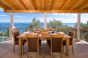 Ein Holztisch mit Stühlen für vier Personen, mit Blick auf eine schöne Landschaft aus Meer und Hügeln.