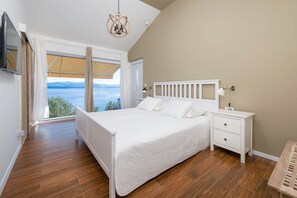 Ein Schlafzimmer mit Bett, Nachttischen, Meerblick und einer Deckenleuchte.