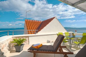 Un balcon avec vue sur la mer, une chaise, une table et un pot de fleurs.