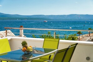 Un balcon avec une table dressée pour le dîner, offrant une vue sur la mer et les bateaux, avec des montagnes qui se dessinent à l’horizon.