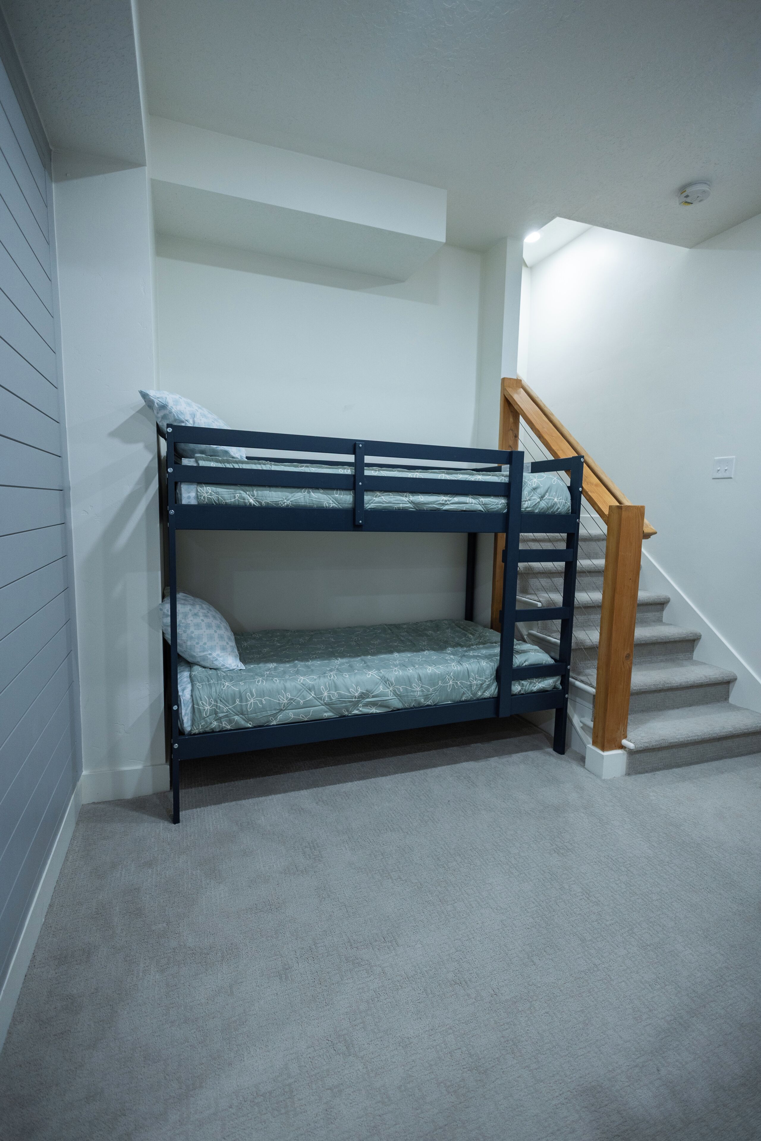 A bunk bed in a room with a staircase and a light switch on the wall.