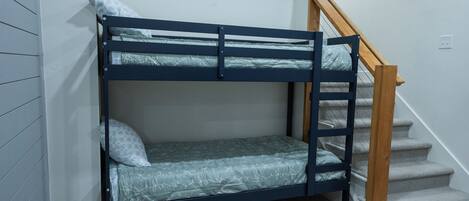A bunk bed in a room with a staircase and a light switch on the wall.