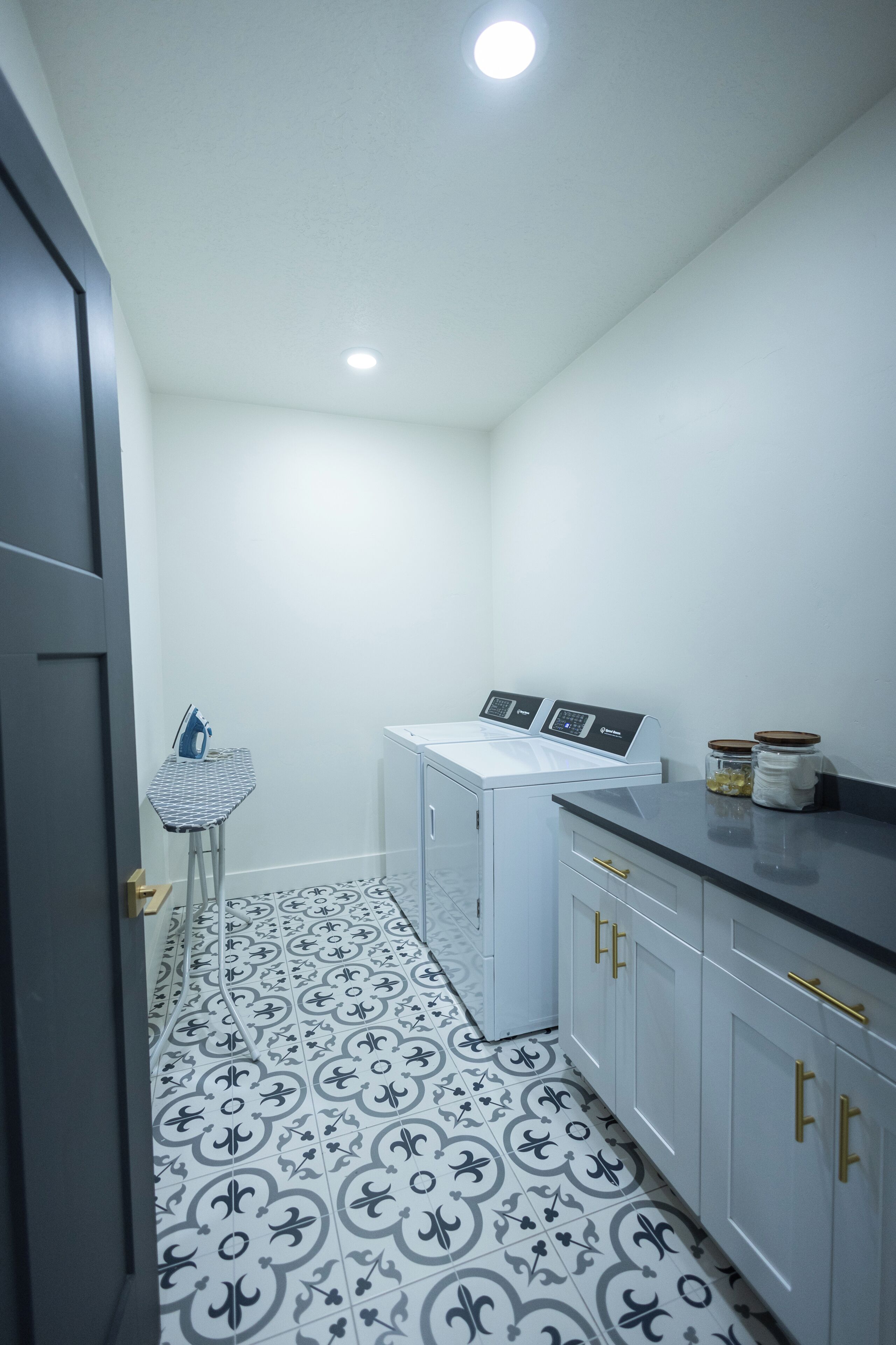A laundry room with a washing machine, ironing board, and cabinets.