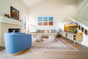 A living room with a sofa, ottomans, a fireplace, a TV, and artwork on the wall. - Carmel Valley Gem - Pool, Tennis & Garage (San Diego)