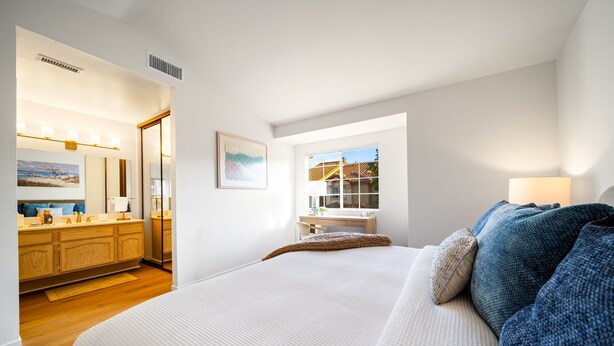 A bedroom with a large bed, a bedside table, a window, and a bathroom visible in the background. - Carmel Valley Gem - Pool, Tennis & Garage (San Diego)