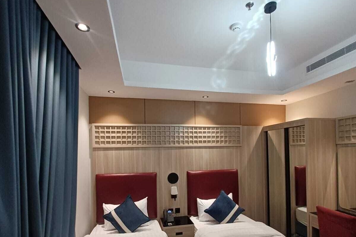 A hotel room with two beds, a nightstand, a mirror, and a ceiling light.