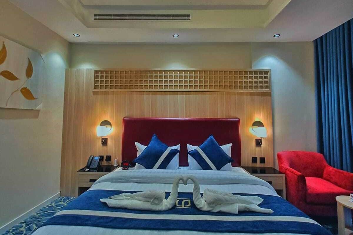 A hotel room with a large bed, two bedside tables, a red armchair, and a ceiling light fixture.