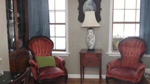 A room with two red upholstered chairs, a wooden side table, a glass cabinet, and a patterned rug. - Armory Quarters B (Bolivar)